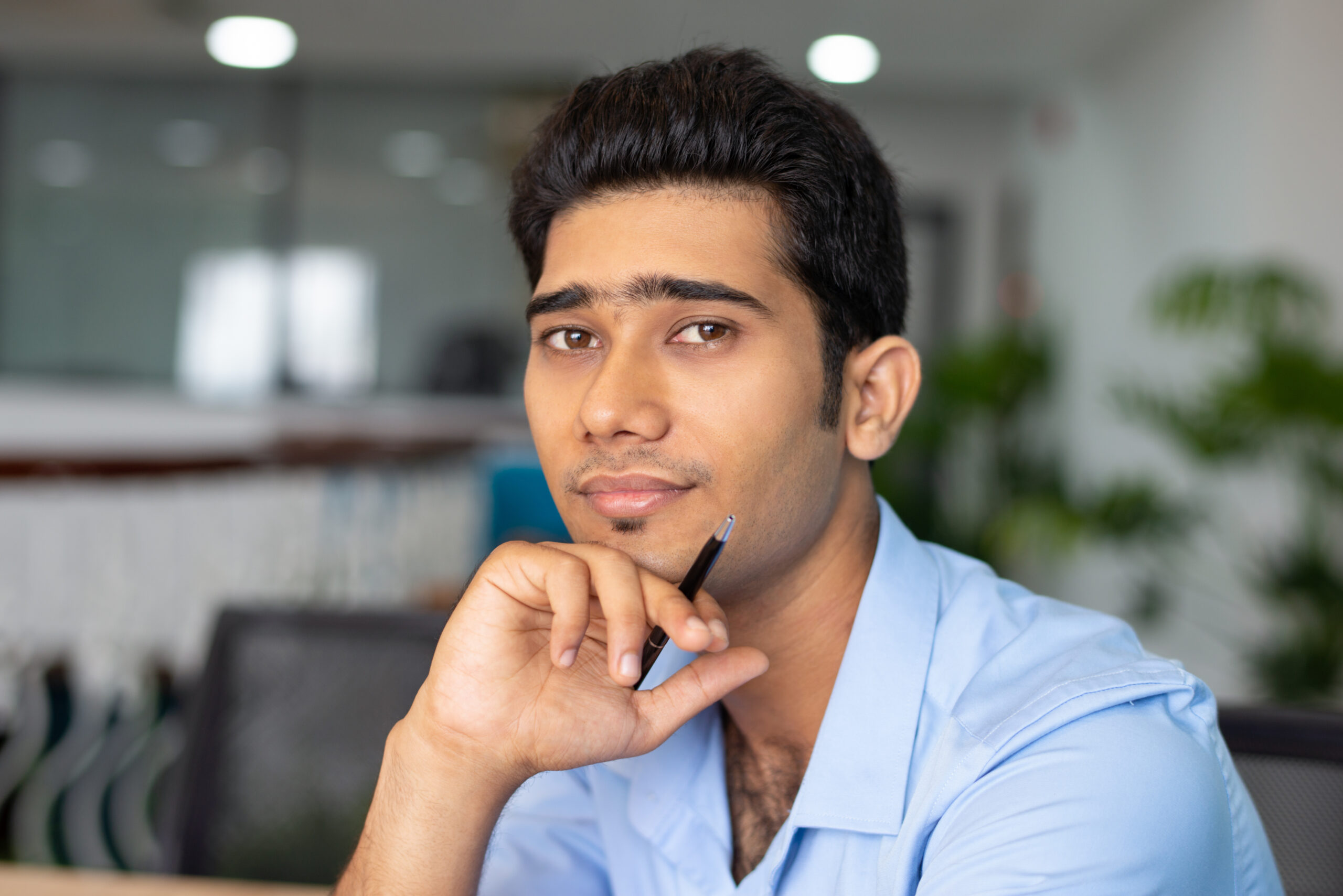 Portrait of young Indian businessman or student sitting with pen Portrait of young Indian businessman or student sitting with pen and looking at camera in office. Businessman concept